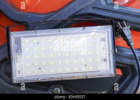 Industrial rectangular led floodlight panel resting on orange vehicle plastic bumper ready for outdoor construction work showing sturdy reliable desig Stock Photo