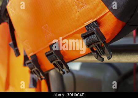 Closeup detail of bright orange waterproof dry bag fabric with secure black plastic buckle and strap showing durability for tough outdoor adventure an Stock Photo