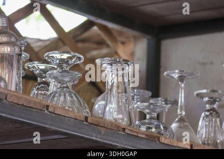 Clean empty clear glass cup and goblet collection arrange on wood shelf rack in rustic restaurant kitchen with organized and neat emotional expression Stock Photo