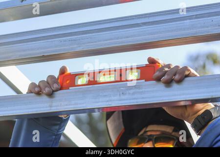 Close up professional construction worker holding orange spirit level on metal beam to check alignment accuracy during focused building inspection wit Stock Photo