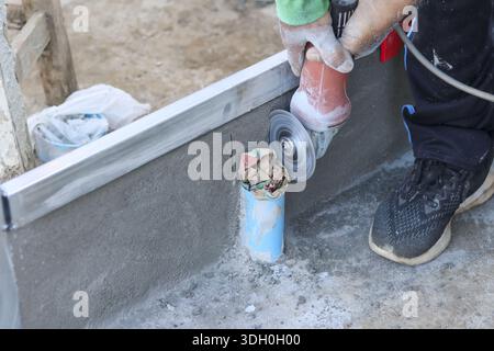 Construction worker carefully cutting blue pvc pipe using angle grinder power tool during renovation process with focused precision on concrete floor Stock Photo