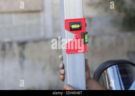 Focused male construction worker holding silver metal pole using red magnetic post level ensuring accurate vertical alignment during fence installatio Stock Photo