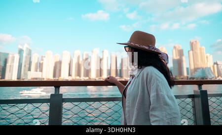 woman standing by waterfront overlooking city skyline from Bluewater island Dubai, Dubai Ain, JBR beach walk, Dubai Marina Stock Photo