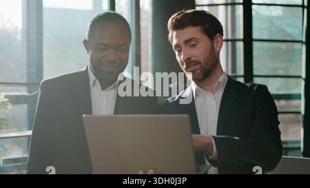 Diverse business team men colleagues cooperation with laptop online internet using web cyberspace work in office talking partners multiracial Stock Photo