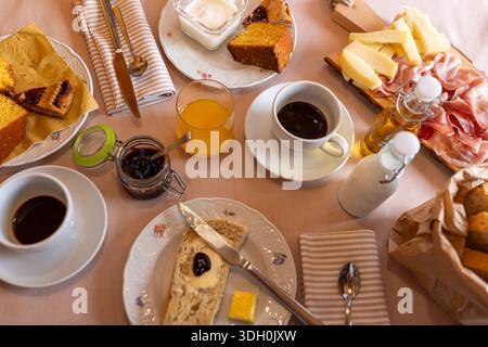 Set table with coffee, croissants, eggs, bread, cold cuts, and fruit. Italian flavor mix. Stock Photo