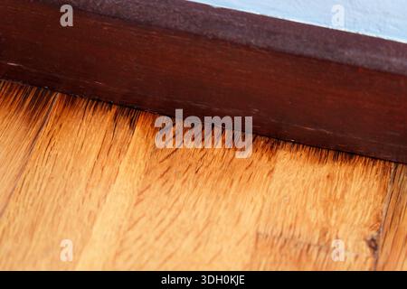 Floor rot with black stains on laminate panels next to wooden baseboard along blue wall Stock Photo