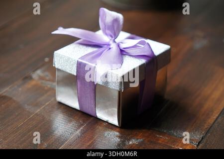 Sparkling silver gift box with lavender ribbon bow placed on rustic wooden tabletop Stock Photo