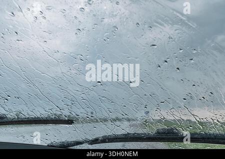 Raindrops on car windshield with wipers and cloudy sky background Stock Photo