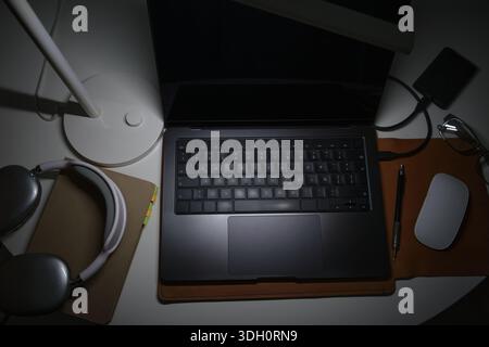 Desk lamp providing focused light on a laptop and accessories in a personal workspace at night Stock Photo