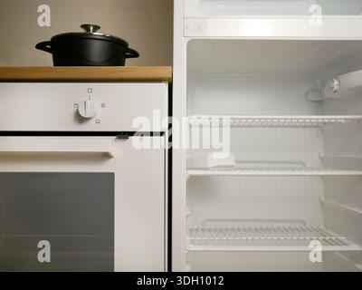 Modern minimalist kitchen interior with an open empty refrigerator and a built-in oven and a cooking pot on the stove. Clean white household appliance Stock Photo