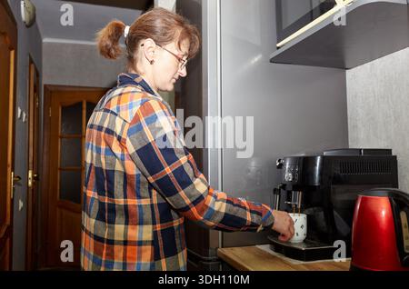 Woman turning on coffee machine while preparing morning drink in kitchen. Woman preparing fresh aromatic coffee with modern machine at home Stock Photo