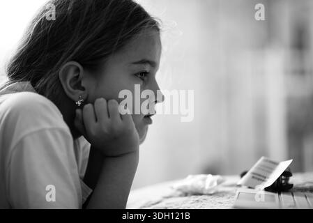 Thoughtful child watching educational content on digital device at home Stock Photo
