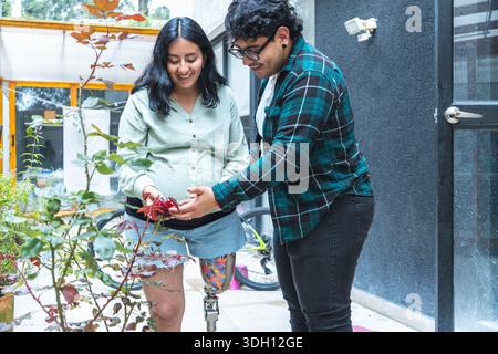Pregnant woman with a prosthetic leg gardening with her partner, enjoying a peaceful moment together Stock Photo