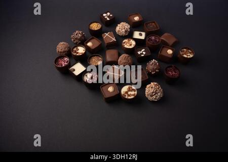 assorted artisanal chocolate pralines and truffles arranged on matte black surface, rich dark and milk tones, glossy ganache, textured nuts and sprink Stock Photo