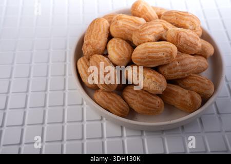 pile of small golden-brown choux pastries and mini eclairs in a shallow ceramic bowl on a white tiled tabletop, showcasing ridged shells and warm tone Stock Photo