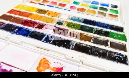 White plastic box with watercolor paints. Opened paint set for professional watercolor paint on white background. Used paint collection close up. Art Stock Photo