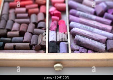 Red and lilac soft pastel pieces in a wooden box with dividers. Art supplies are arranged by tone and ready to use. Art creativity concept Stock Photo
