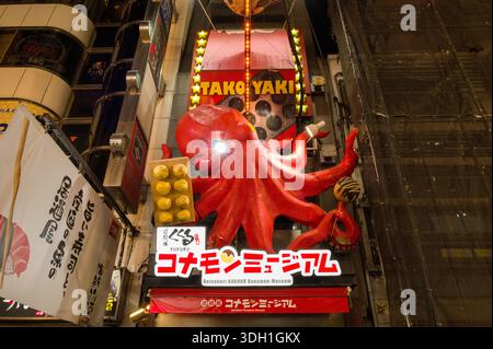 Osaka, Japan - November 5, 2023: Large red octopus sculpture and illuminated takoyaki sign above the entrance of the Dotonbori Konamon Museum, with Japanese writing and neighboring storefronts visible at night. Stock Photo