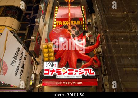 Osaka, Japan - November 5, 2023: Large red octopus sculpture and illuminated takoyaki sign above the entrance of the Dotonbori Konamon Museum, with Japanese writing and neighboring storefronts visible at night. Stock Photo