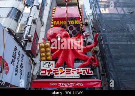 Osaka, Japan - November 5, 2023: A large red octopus sculpture holding takoyaki balls is mounted above the entrance of a restaurant in the Dotonbori district, with Japanese signage and neighboring buildings visible. Stock Photo