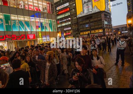 Osaka, Japan - November 5, 2023: Large crowd of people gathered on a city street at night in Osaka, with uniformed police officers standing in a line and illuminated commercial signage visible in the background. Stock Photo