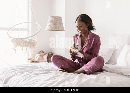 Black Female Taking Notes Writing In Notebook Sitting In Bedroom Stock Photo