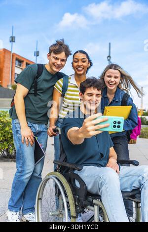 Group of happy diverse university students, including a person using a wheelchair, smiling and taking a cheerful selfie together on campus, representi Stock Photo
