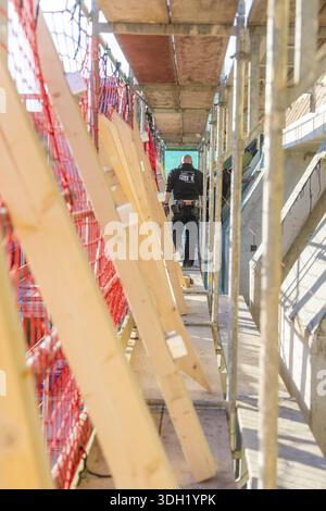A worker walks over scaffolding surrounded by wooden boards and a protective net in a bright environment, carpentry construction, roof extension, reno Stock Photo