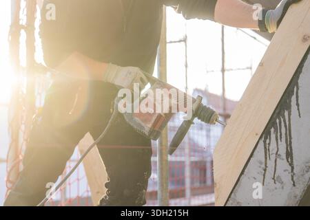 Construction worker drilling wood elements on construction site in sunlight, carpentry construction site, roof extension, renovation, Stuttgart, Germa Stock Photo