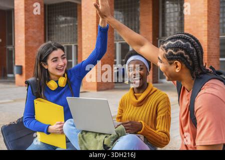 Diverse group of university students collaborating, celebrating a successful academic achievement with a high five, expressing joy and teamwork on cam Stock Photo