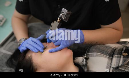 Close up view of a beautician applying permanent eyeliner makeup to a woman's eyelid. Professional cosmetic procedure in a beauty salon Stock Photo