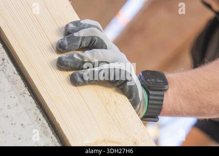 Close-up of a gloved hand holding a wooden plank, carpentry construction, roof extension, renovation, Stuttgart, Germany Stock Photo