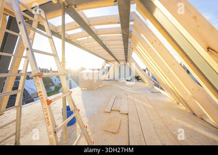 An unfinished wooden roof truss on a construction site, illuminated by sunlight. A ladder is ready, carpentry construction site, roof extension, renov Stock Photo