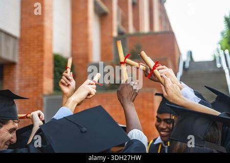 Diverse group of university students wearing graduation caps and gowns, celebrating their achievement and success while holding their diplomas joyfull Stock Photo