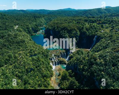 Aerial view of cascading waterfalls plunge into turquoise pools, embraced by dense, emerald forests in Plitvice Lakes National Park, Plitvice Lakes Na Stock Photo