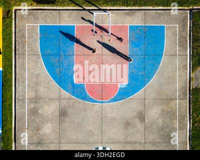 Aerial view of figures cast long shadows on a brightly colored basketball court with vivid blue and red contrasts, Shuri, Bumthang, Bhutan. Stock Photo