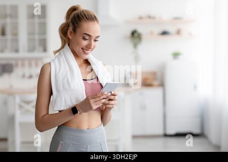 Happy european cute millennial blonde female checking fitness app or social media on smartphone Stock Photo