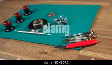 A watchmaker prepares tools for the repair of a mechanical watch on a green surface with various instruments. Stock Photo