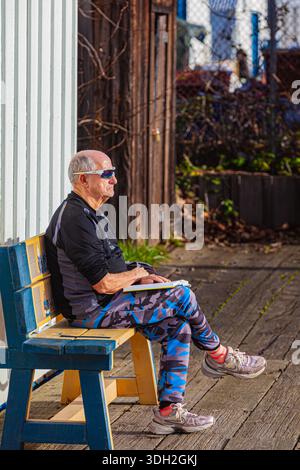An older gentleman reading a book in the January sunshine in Steveston B.C. Canada Stock Photo