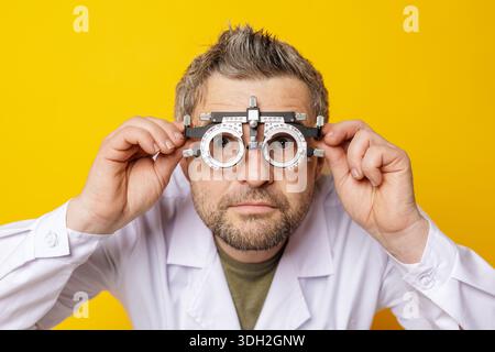Closeup of male eye doctor holding trial frame during refraction test for glasses or contact lens prescription on yellow background Stock Photo