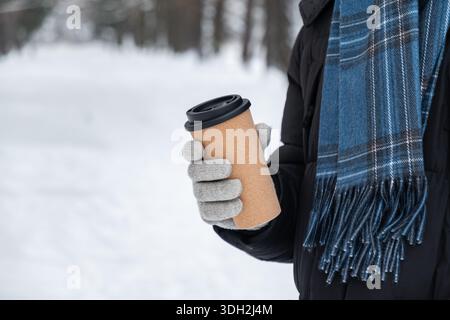 Close up of reusable coffee cup in hands of young adult man wearing winter jacket and scarf outdoors. Stock Photo