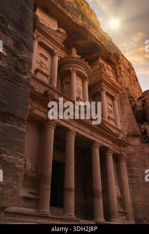 The ancient structure in Petra stands tall as the sun sets, casting shadows on its intricate design. Tourists gather around to admire the historical s Stock Photo