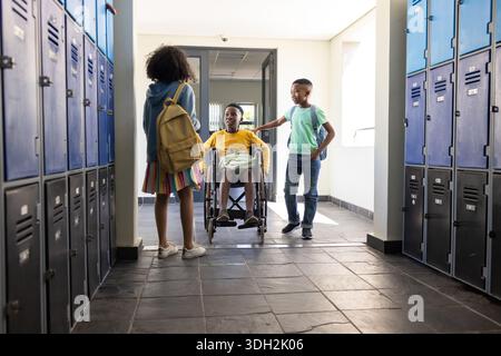 African American students supporting wheelchair student, holding backpacks and notebooks in hallway Stock Photo