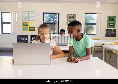Diverse teenage classmates collaborating in classroom, female youth focusing on laptop screen Stock Photo