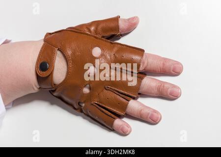 Close-up of a woman's hand in a stylish brown leather glove with distinctive holes and a buttoned cuff against a plain white background. The glove's s Stock Photo