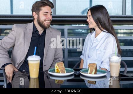 Young man and woman smiling and talking while sitting at an outdoor cafe Stock Photo
