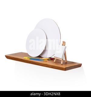 Paintbrushes and blank canvases on an oak wooden shelf, isolated on a white background, authentic photograph, not AI-generated Stock Photo