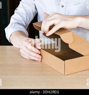Close view of fingers prying open the lid of an empty cardboard box on desk. Stock Photo