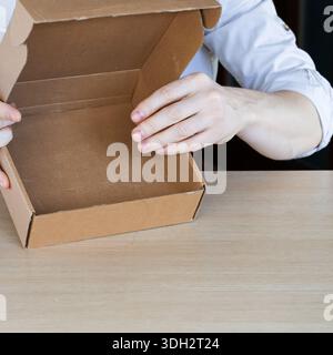 Close-up of hands holding open empty brown cardboard box over wooden table, revealing nothing inside. Stock Photo