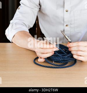 Close-up of person's hands grasping braided blue instrument cable with metal jacks on wooden surface Stock Photo
